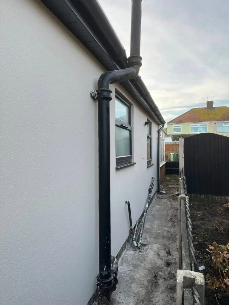 House render side elevation with new white render and black downpipe